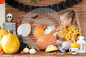 Girl in witch halloween costume sitting on a table playing with pumpkin and her pet cat. Halloween lifestyle background.