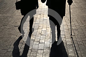 Girl and woman with a cane, black silhouettes and shadows of two people walking on the street