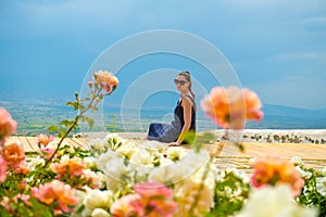 Girl or woman sits on a terrace with a panoramic view of the mountains with pink roses rosebuds in the foreground