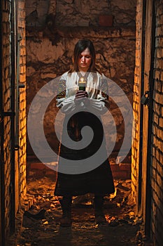 A girl, a woman in traditional Ukrainian clothing stands in a dark basement with a candle in her hands. Tragedy in Ukraine, war of