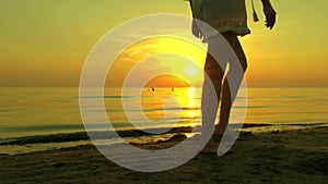 Girl woman is walking along a sandy sea beach barefoot on a sunset background. The girl is walking in slow motion, the