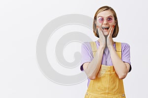 Girl won tickets to music festival, standing in cute yellow overalls and sunglasses, smiling joyfully and gazing amazed