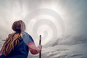 Girl with a wooden stick looking into the clouds