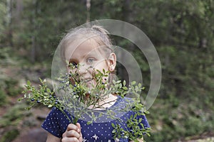 Girl in the woods with a sprig of blueberries looks at the camera