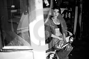 Girl worker in overalls stands in workshop near opened capote of photo