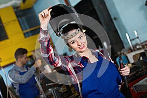 Girl worker is standing in protection helmet in workshop.