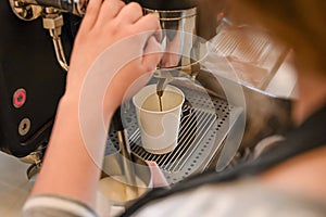 Girl workin on professional espresso cafe machine in cafeteria with white cup to take off