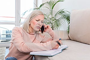 Girl working from home, talking on the phone and writing notes in her note book. Entrepreneur or student working or studying at