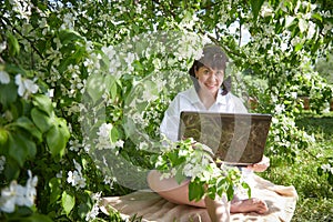 Girl Working on Laptop in Blossoming Garden. Middle aged woman using computer in white apple blossoms. Female freelancer