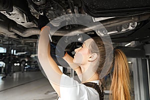 Girl working undercarriage of automobile, using tool.