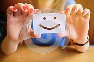 Girl works holding a piece of paper with a smiley face. The concept of a good mood