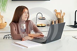 The girl works in the kitchen, work online. Young woman with a laptop and a glass of wine