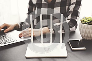 Girl works at the laptop with the phone in hand near white wi fi router in office. iot