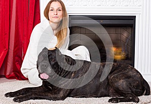 Girl wrapped in a blanket sits near the fireplace with dog Cane Corso