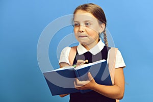 Girl writes in big blue notebook. Pupil in school uniform