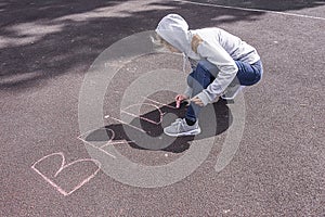 The girl writes chalk on the asphalt