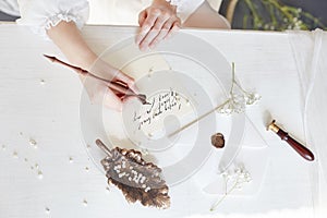 Girl writes a letter to her beloved man, sitting at home at table in a white light dress, purity and innocence. Curly blonde