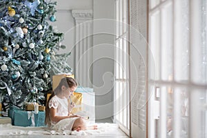 Girl writes a letter to Santa Claus in a large and bright room with a Christmas tree in blue and gold colors