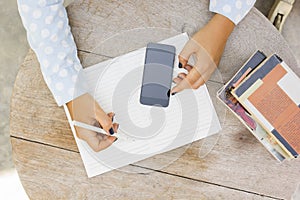 Girl writes in a notebook, with cell phone and books