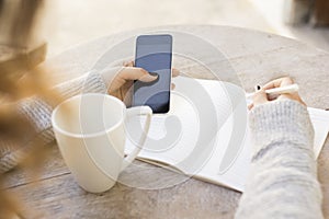Girl writes in a notebook, with cell phone and cup of coffee