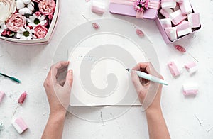 Girl writes in open notebook on table with flowers and marshmallows,pastel colors.Beauty Flat lay.Copy space.Eye bird view.