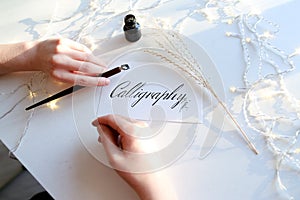 Girl writes pen fountain calligraphic letters, sitting at table