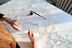 Girl writes pen fountain calligraphic letters, sitting at table