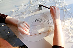 Girl writes pen fountain calligraphic letters, sitting at table