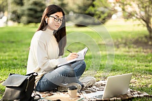 Girl writing in diary, sitting in parkland