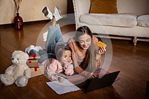 Girl writing wishlist, happy mother using pc and credit card