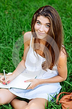 Girl writting in a notebook sitting in the grass