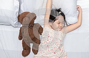 Girl yawn and sleep on bed with teddy bear doll