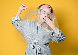Girl yawning. Sleepy young woman yawns, model wearing nightie - night dress,  on yellow background. Studio shot