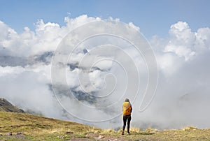 Girl with yellow backpack hiking in the Pyrenees, with the mountains in the clouds in the background
