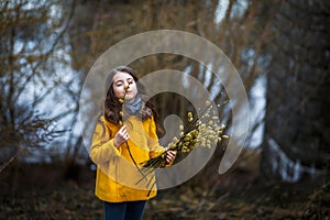 A girl in a yellow coat in the forest in early spring with a willow branch of twigs. A girl furing freshet or high water