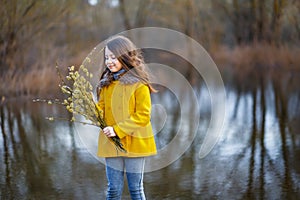 A girl in a yellow coat in the forest in early spring with a willow branch of twigs. A girl furing freshet or high water