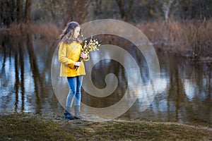 A girl in a yellow coat in the forest in early spring with a willow branch of twigs. A girl furing freshet or high water