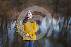 A girl in a yellow coat in the forest in early spring with a willow branch of twigs. A girl furing freshet or high water