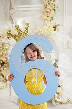 A girl in a yellow dress holds a large number 6.With a Golden crown. The Princess birthday party.