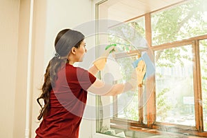 Girl in yellow gloves with a detergent washes plastic windows. Cleaning company for home and window cleaning