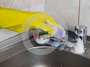 A girl in yellow gloves washes the faucet in the kitchen, close-up