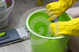 A girl in yellow gloves wets a rag in a bucket, cleaning equipment domestic