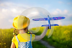 Girl in a yellow hat launches a toy plane into the field, looks at the trail. Summer time, childhood, dreams and carelessness. Air