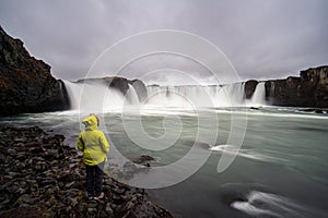 Girl in yellow hiking jacket infront of Godafoss waterfall near Akureyri in the Icelandic highlands.