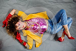 The girl in a yellow jacket and blue jeans with an afro hairdo lies on the floor. Fashion eighties, the era of disco.