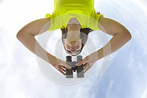 Girl in a yellow jacket looking through binoculars against the sky