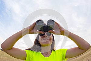 Girl in a yellow jacket looking through binoculars against the sky