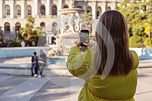 A girl in a yellow jacket, a view from the back, takes a photo on the phone outside the door.
