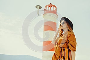 A girl in a yellow-orange suit on the beach against the background of the sea, mountains and a lighthouse. Fashionable woman in