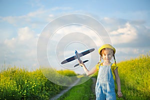 Girl in a yellow panama hat launches a toy plane into the field. Summer time, happy childhood, dreams and carelessness. Air tour photo